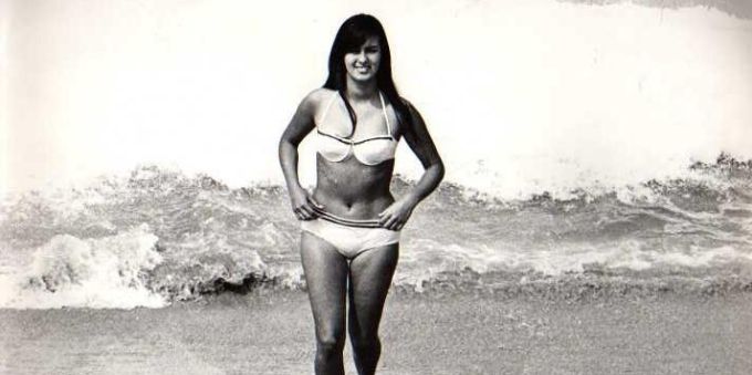 Na imagem temos a foto da famosa garota da praia de Ipanema, a fotografia é em preto e branco, e nela uma mulher está saindo do mar que está ao fundo.