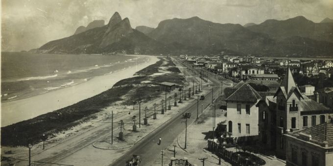 Na imagem temos a fotografia da região da praia de Ipanema no passado. A foto é em preto e branco e é possível ver a a praia, o pão de açúcar, e algumas casas.