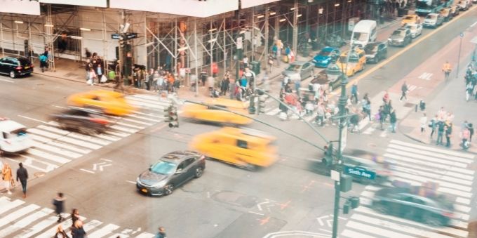 Nova York: imagem desfocada mostra cruzamento, com carros passando rápido e muitas pessoas na rua 