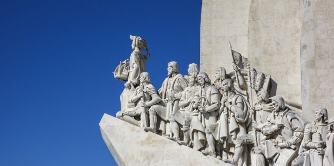 Imagem a ceú aberto de monumento de pedra mostrando desbravadores, como forma de homenagem, em Lisboa 