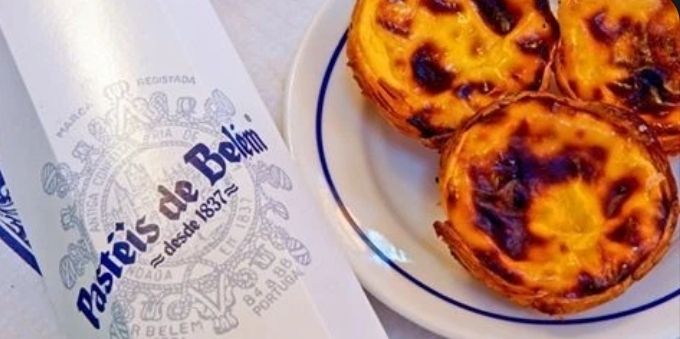 Imagem fechada mostra prato com pastéis de Belém ao lado de guardanapo, em Lisboa