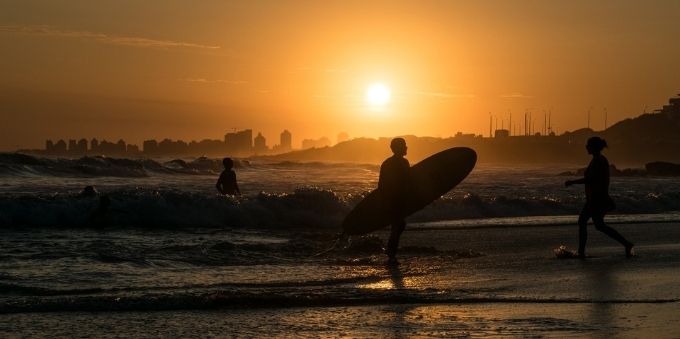 Imagem mostra silhueta de surfista saindo do mar, em Punta Del Leste. 