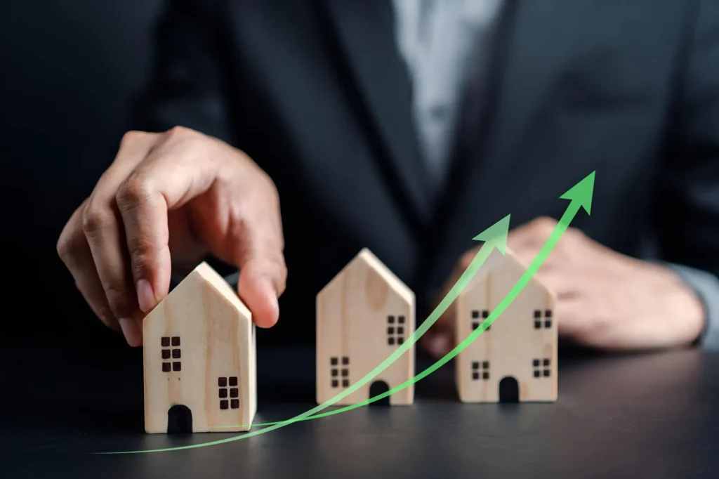Um investidor segura miniaturas de casas, enquanto aparece uma seta verde que indica subida de preço, para ilustrar a valorização imobiliária.