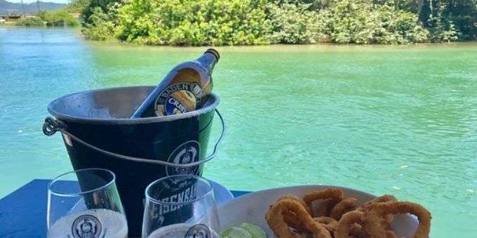 Imagem mostra balde com gelo e bebidas, em frente de água cristalina em Lagoa da Conceição.